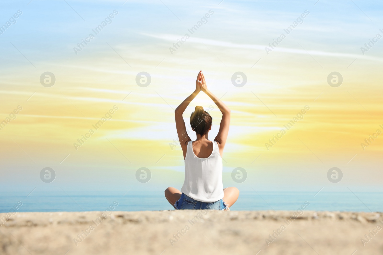 Image of Beautiful young woman practicing yoga near sea at sunrise, back view
