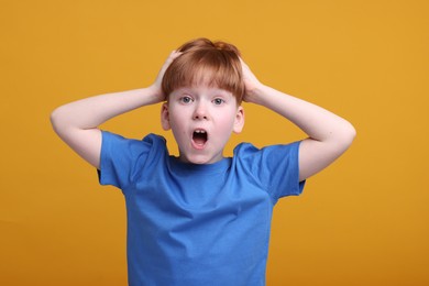 Portrait of surprised little boy on orange background