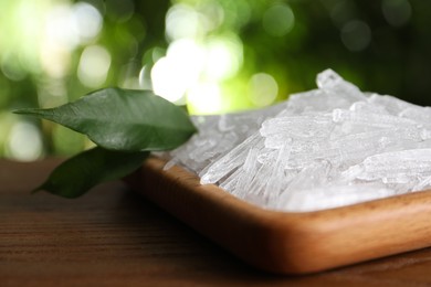 Photo of Menthol crystals and green leaves on wooden table against blurred background, closeup