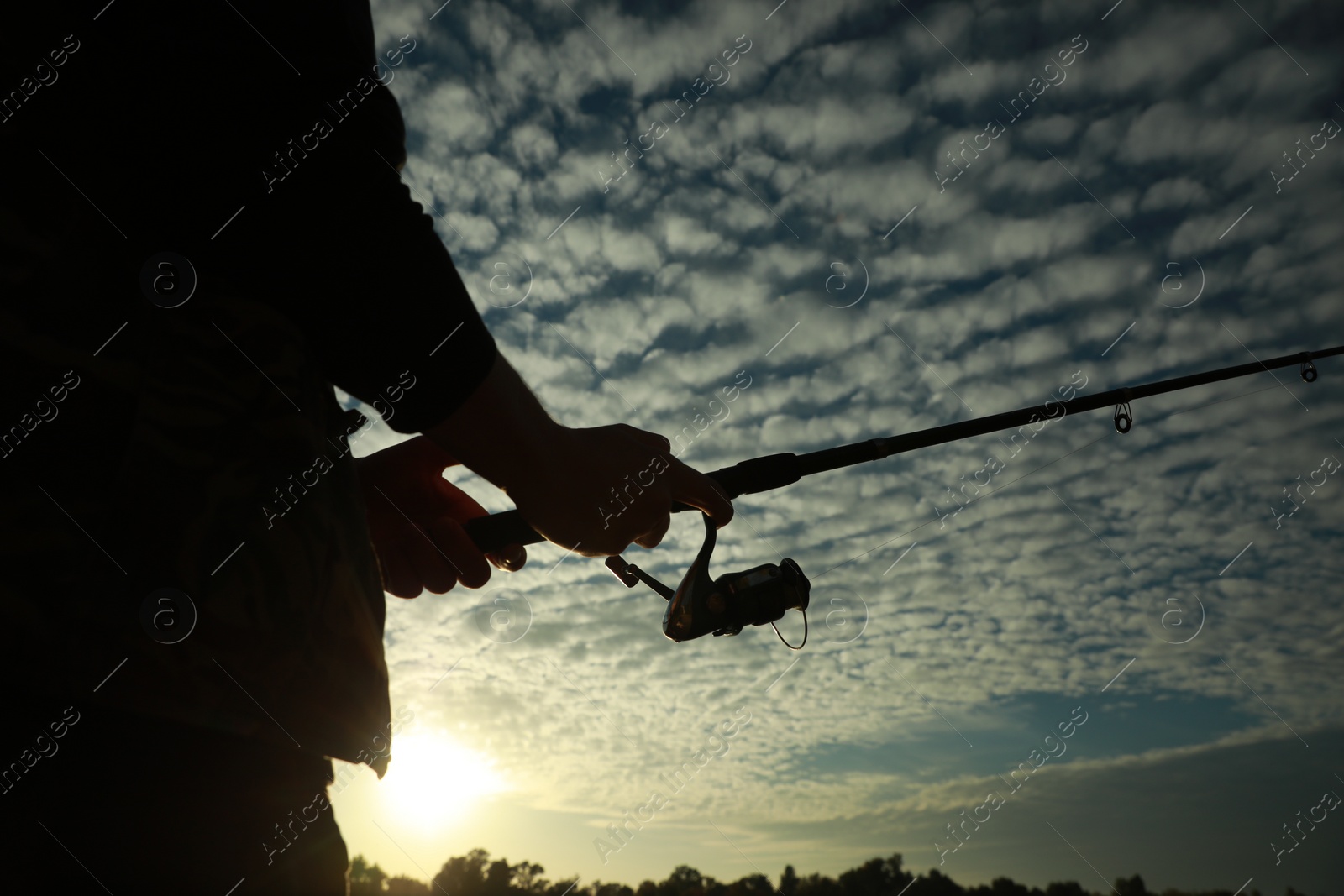 Photo of Fisherman with rod fishing at sunset, closeup