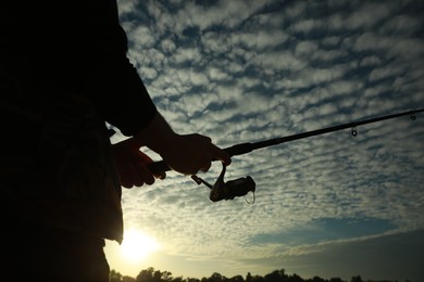 Photo of Fisherman with rod fishing at sunset, closeup