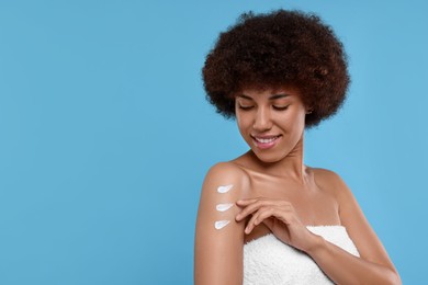 Photo of Beautiful young woman applying body cream onto arm on light blue background, space for text