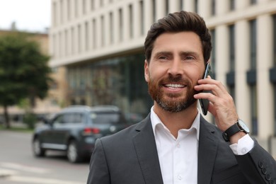 Handsome businessman talking on smartphone while walking outdoors, space for text