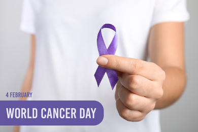 Woman holding purple ribbon against grey background, closeup. World Cancer Day