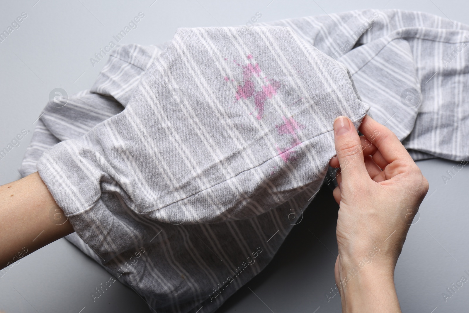 Photo of Woman holding striped shirt with stains on light grey background, top view