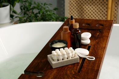 Photo of Wooden board with spa products on bath tub indoors, space for text