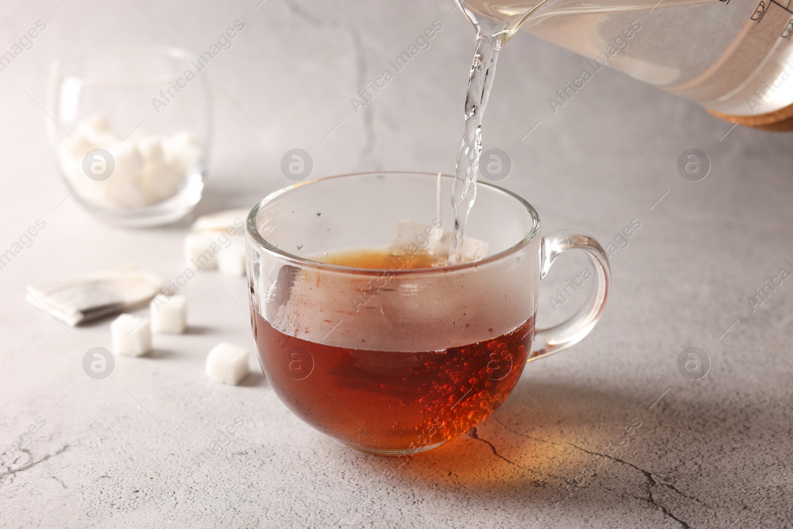 Photo of Pouring hot water into cup with tea bag on light grey textured table, closeup