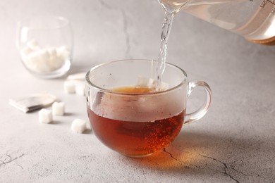 Photo of Pouring hot water into cup with tea bag on light grey textured table, closeup