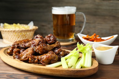 Photo of Delicious chicken wings served with beer on wooden table, closeup