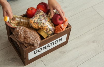 Photo of Woman taking food from donation box on wooden floor, closeup