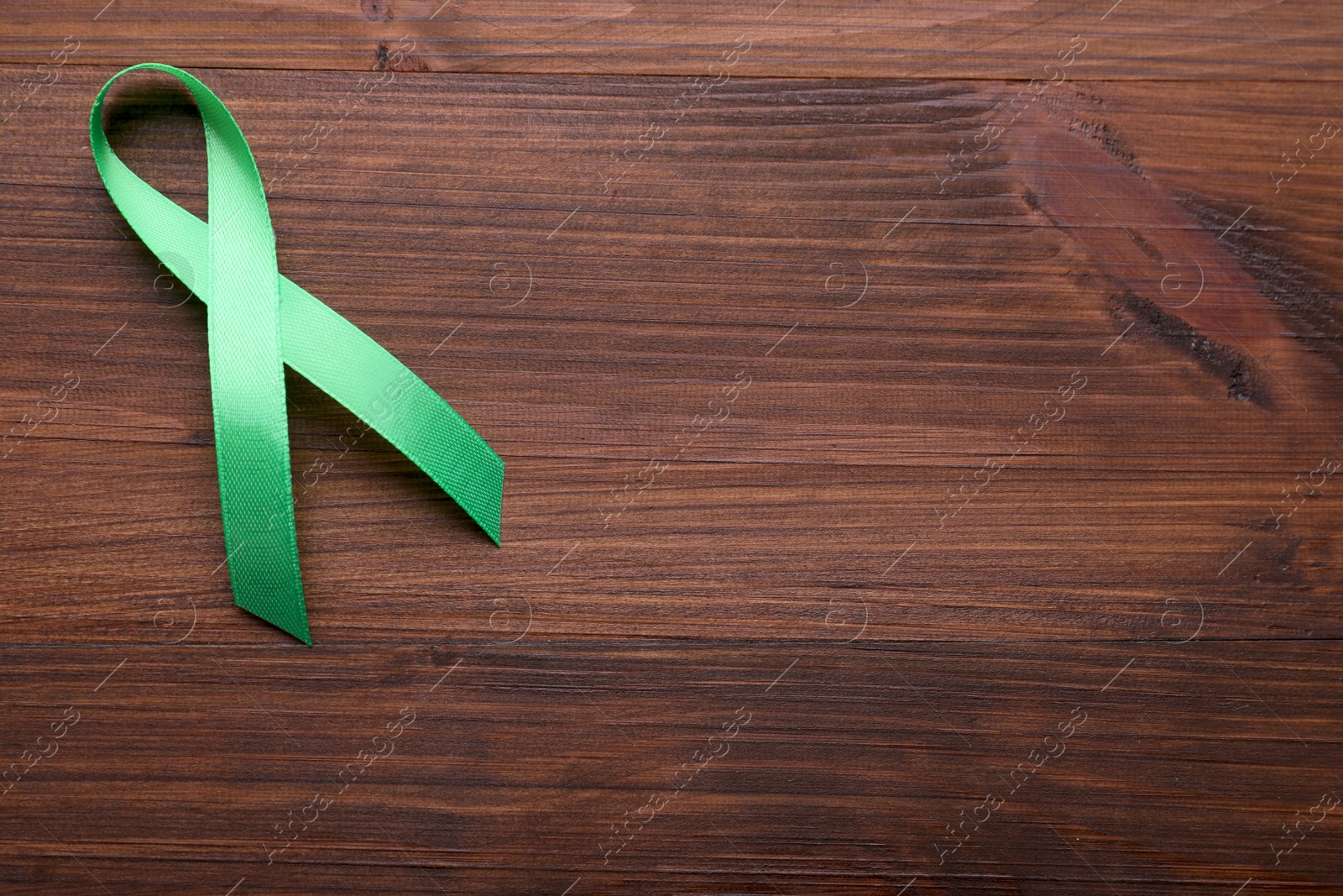 Photo of World Mental Health Day. Green ribbon on wooden background, top view with space for text