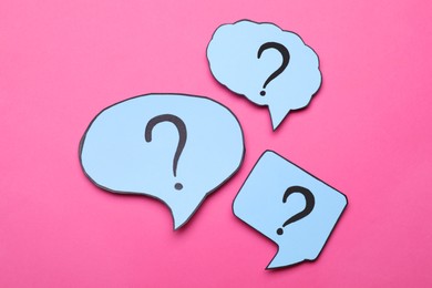 Different paper speech bubbles with question marks on pink background, flat lay
