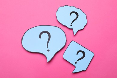 Photo of Different paper speech bubbles with question marks on pink background, flat lay