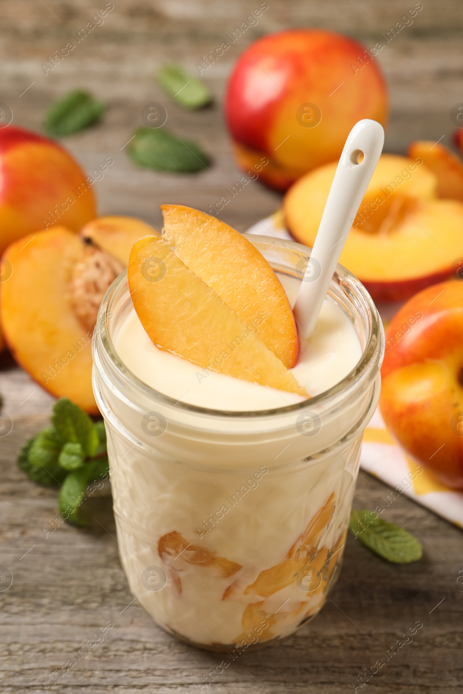 Photo of Tasty peach yogurt with pieces of fruit and spoon in glass jar on wooden table