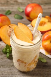 Tasty peach yogurt with pieces of fruit and spoon in glass jar on wooden table