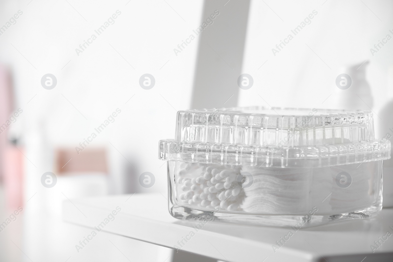 Photo of Container with cotton swabs and pads on white shelf in bathroom. Space for text