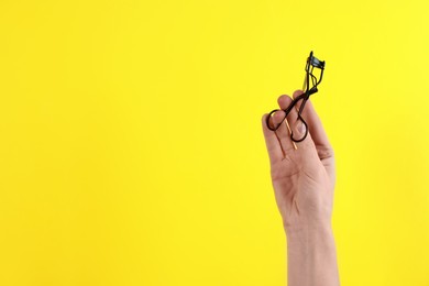 Photo of Woman holding eyelash curler on yellow background, closeup. Space for text