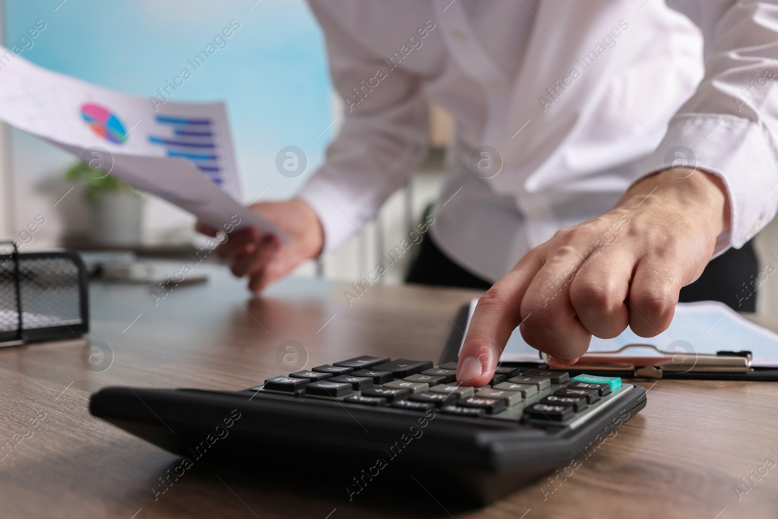 Photo of Man using calculator while working with document at wooden table indoors, closeup