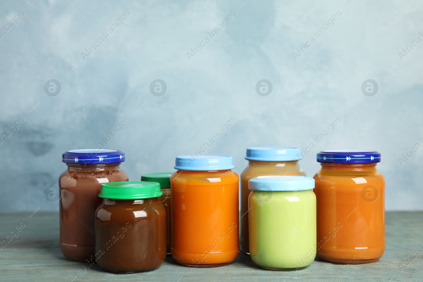 Photo of Jars with baby food on wooden table against light blue background