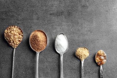 Photo of Spoons with various kinds of sugar on grey background