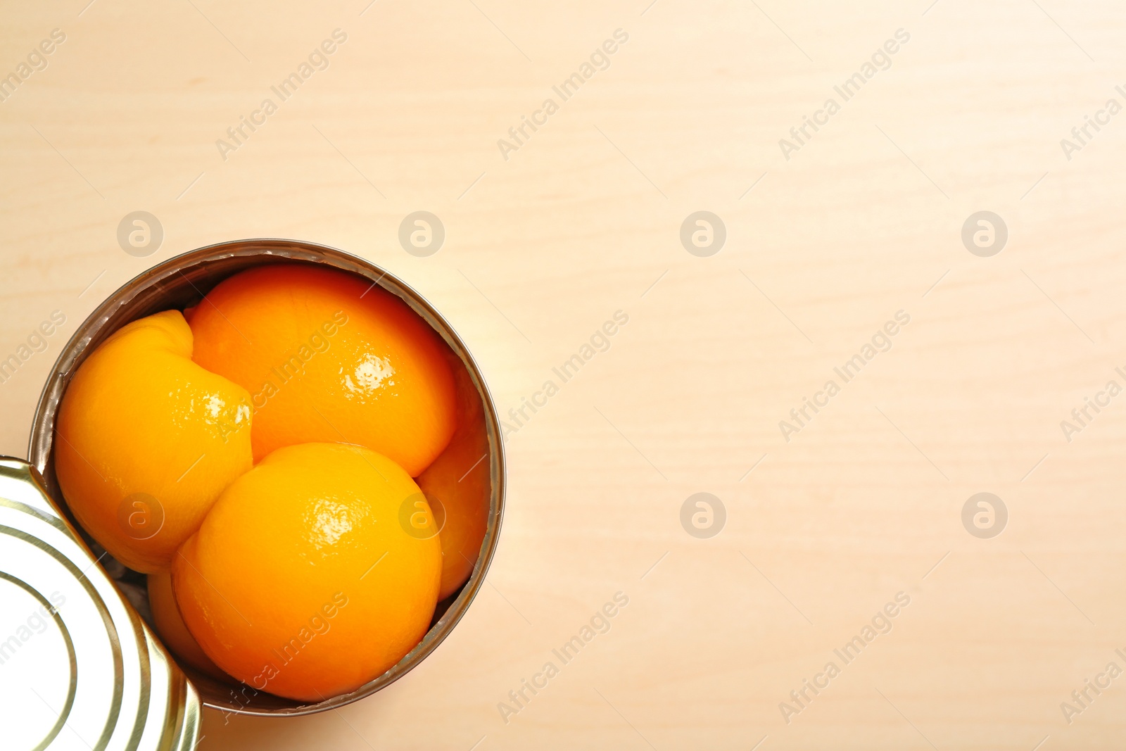 Photo of Open tin can of peaches on wooden background, top view with space for text