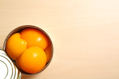 Photo of Open tin can of peaches on wooden background, top view with space for text