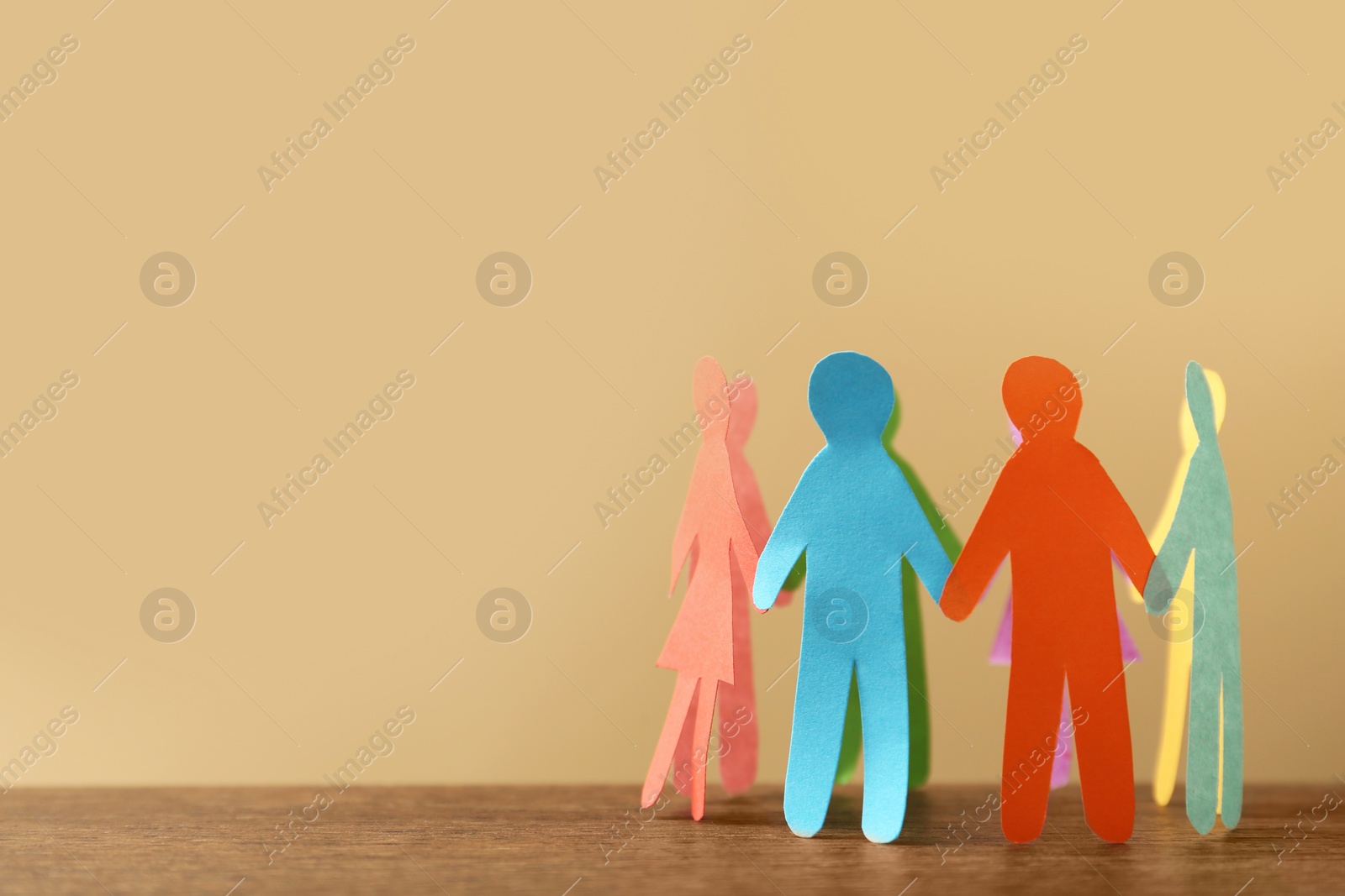 Photo of Many different paper human figures standing in circle on wooden table against beige background, space for text. Diversity and inclusion concept