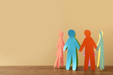 Photo of Many different paper human figures standing in circle on wooden table against beige background, space for text. Diversity and inclusion concept