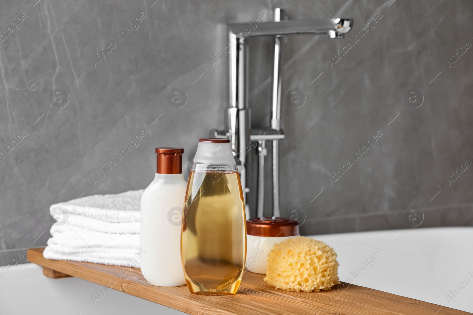 Photo of Wooden bath tray with shampoo, other toiletries and towels on tub indoors