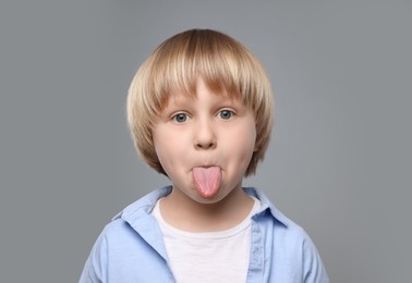 Photo of Cute little boy showing his tongue on grey background
