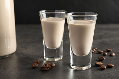 Photo of Coffee cream liqueur in glasses and beans on grey table, closeup
