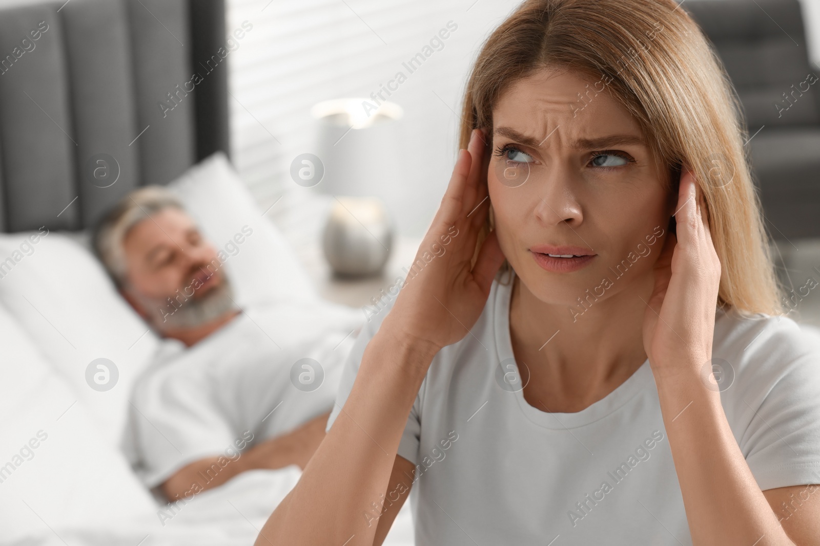 Photo of Irritated woman covering her ears in bed at home. Problem with snoring husband