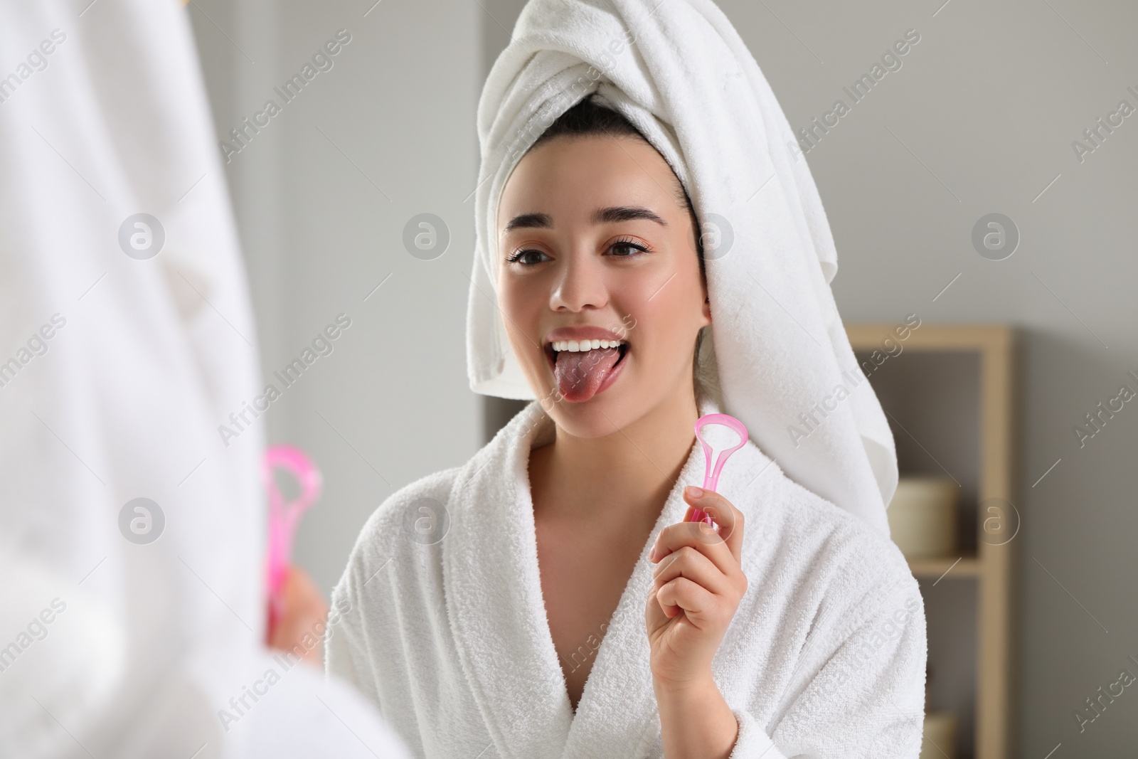 Photo of Happy woman with tongue cleaner near mirror in bathroom