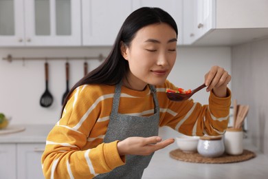 Photo of Beautiful woman cooking and tasting vegetable dish in kitchen