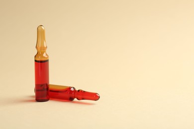 Photo of Glass ampoules with liquid on beige background. Space for text