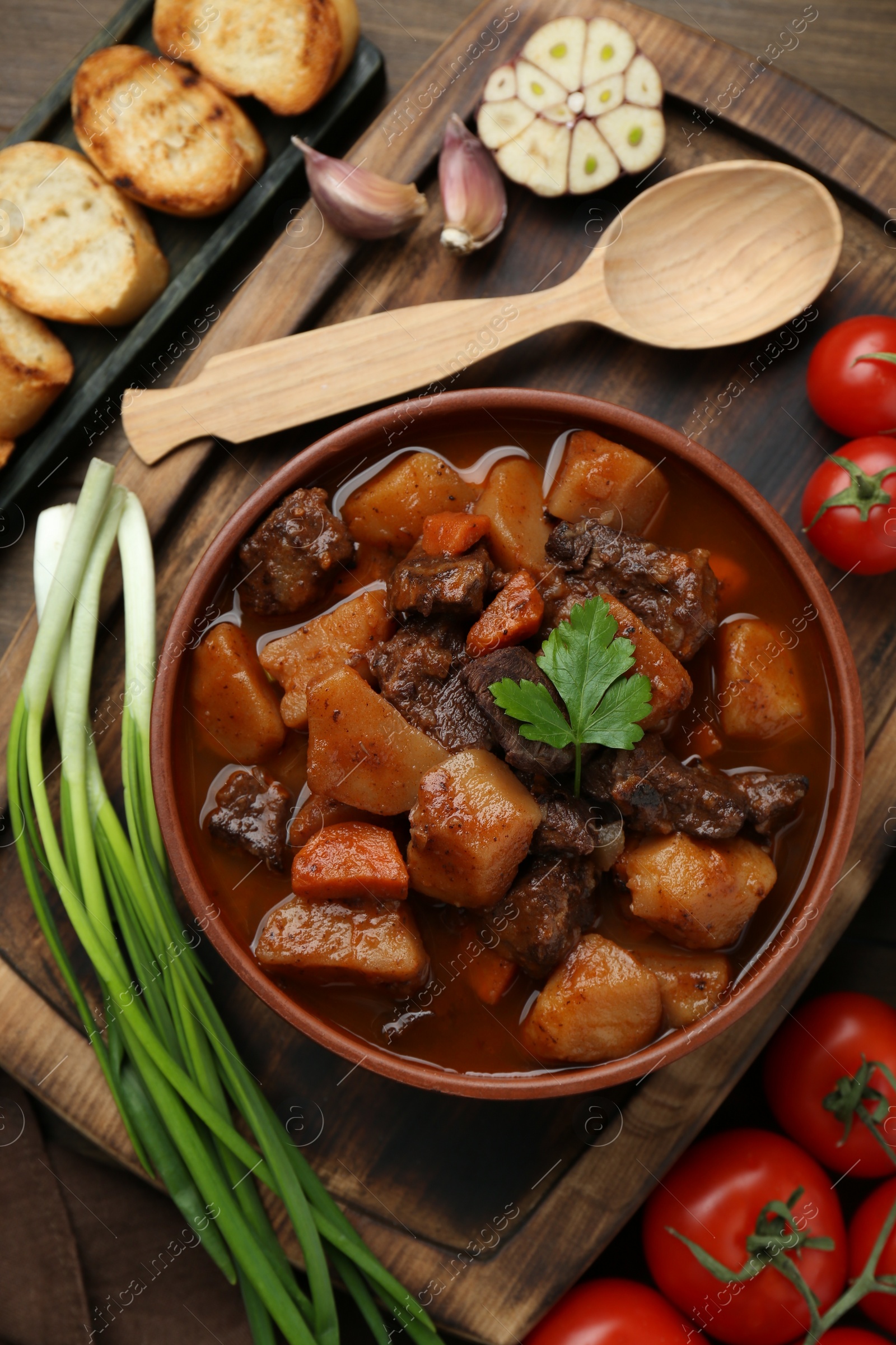 Photo of Delicious beef stew with carrots, parsley and potatoes on wooden table, flat lay