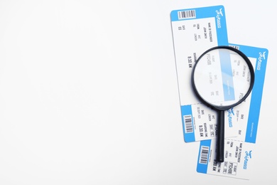 Photo of Avia tickets and magnifying glass on white background, flat lay with space for text. Travel agency concept