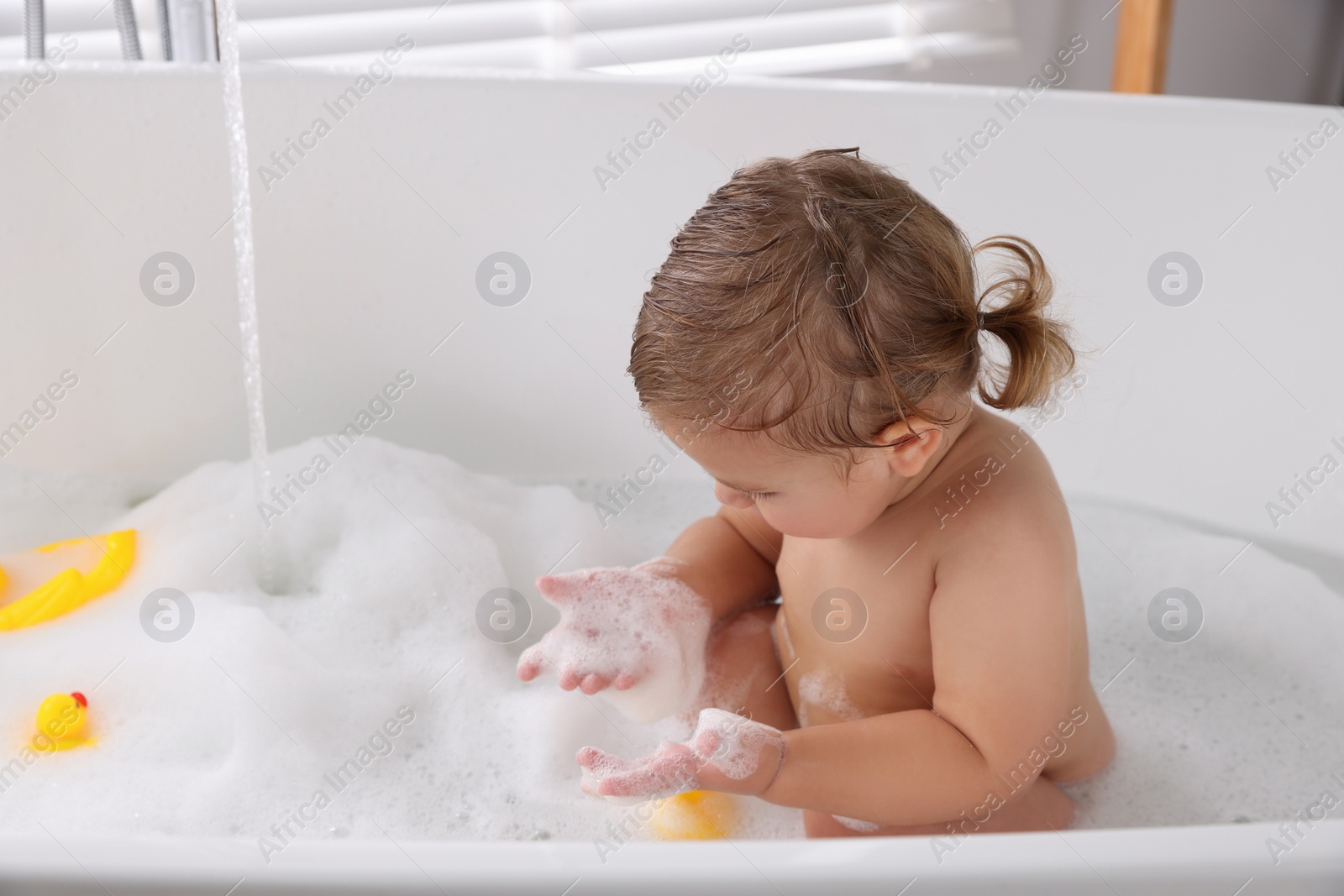 Photo of Cute little girl taking bubble bath with toys indoors