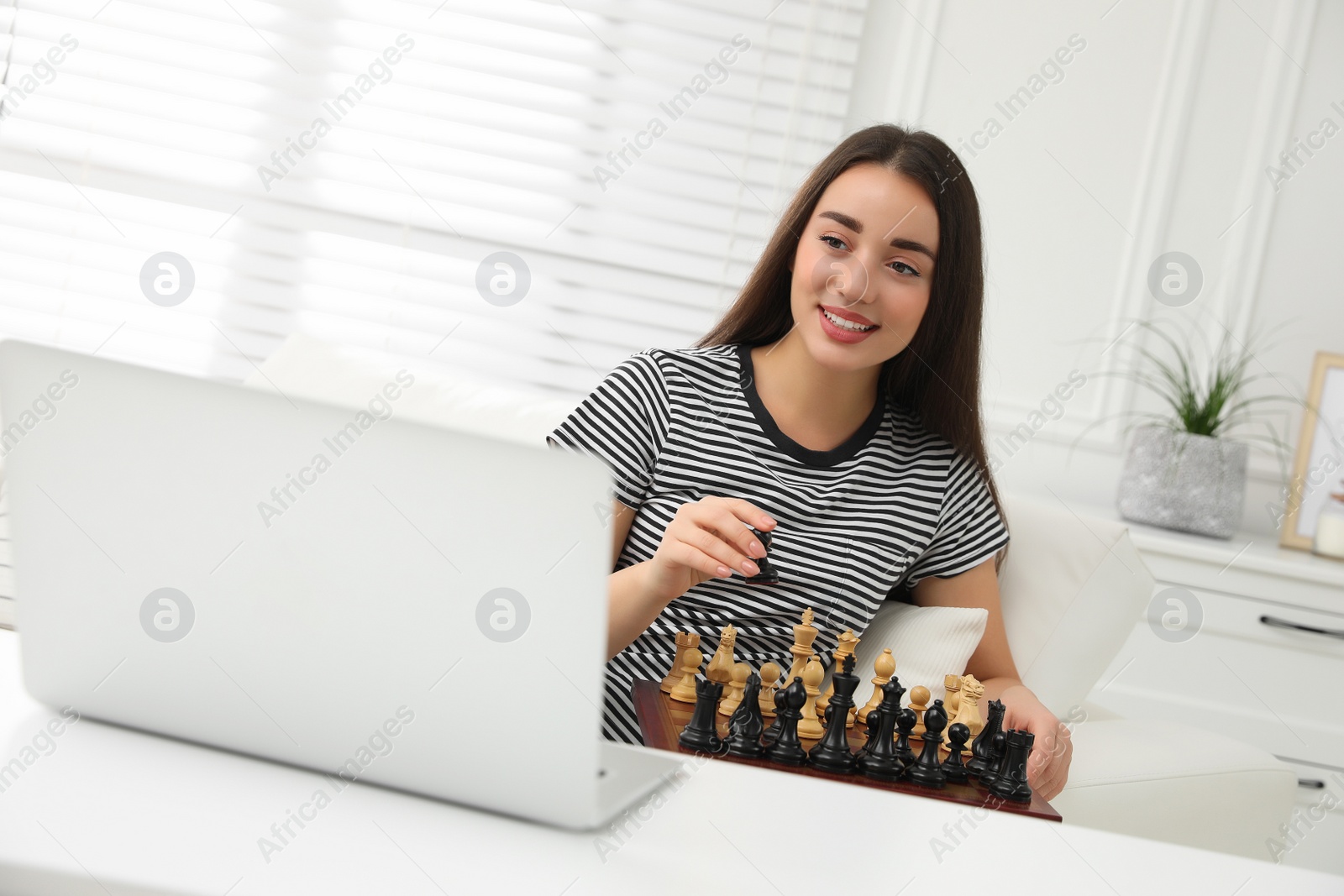 Photo of Young woman playing chess with partner through online video chat at home