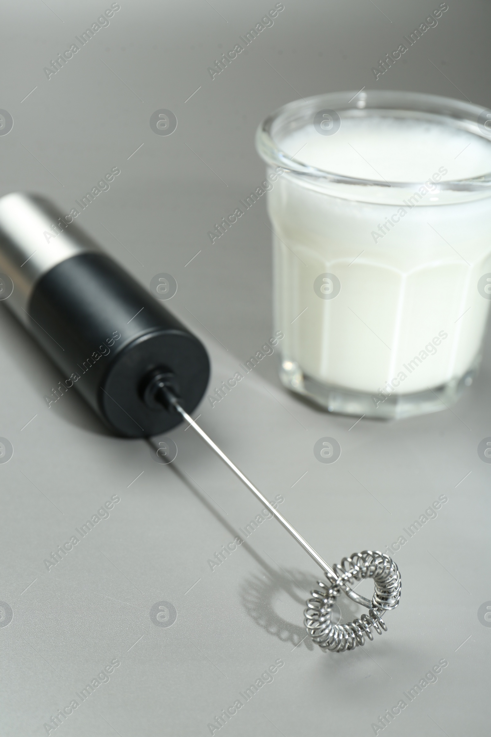 Photo of Mini mixer (milk frother) and whipped milk in glass on grey background