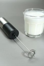 Mini mixer (milk frother) and whipped milk in glass on grey background