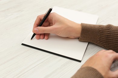 Man writing in notebook at white wooden table, closeup