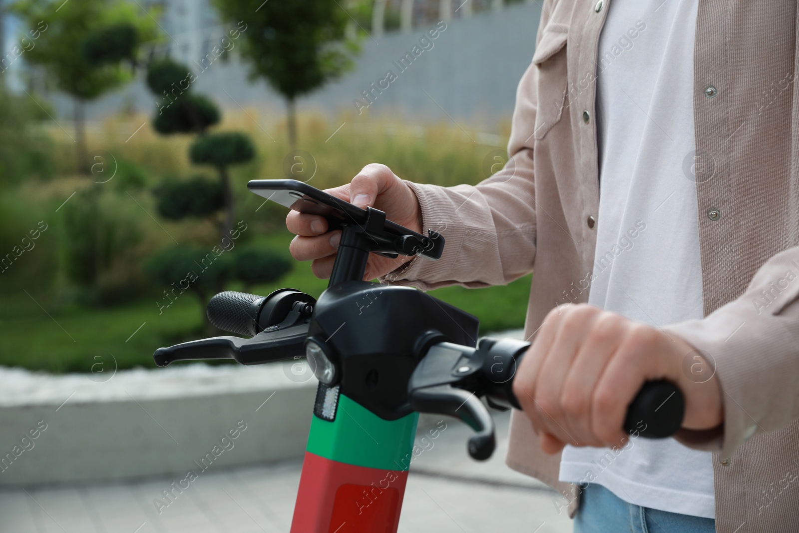 Photo of Man using smartphone to pay and unblock electric kick scooter outdoors, closeup