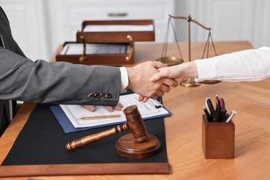 Photo of Notary shaking hands with client at wooden table in office, closeup