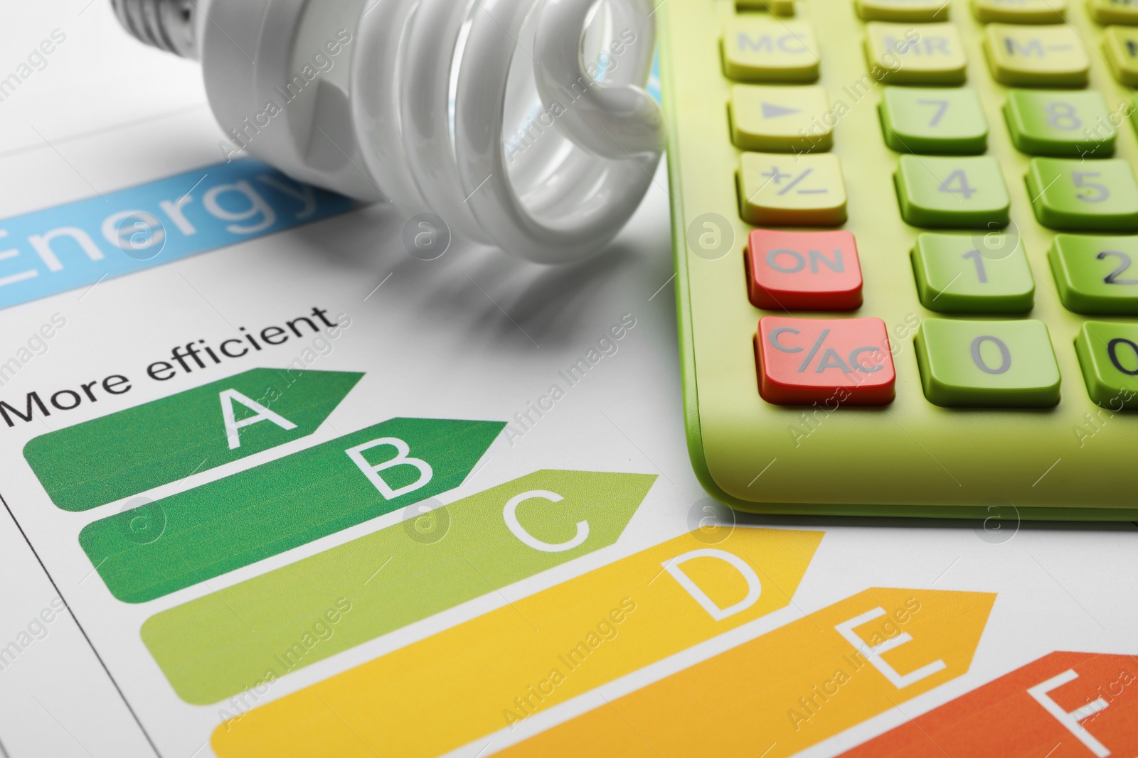 Photo of Energy efficiency rating chart, fluorescent light bulb and calculator, closeup