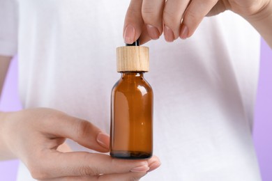 Woman holding bottle with serum against lilac background, closeup