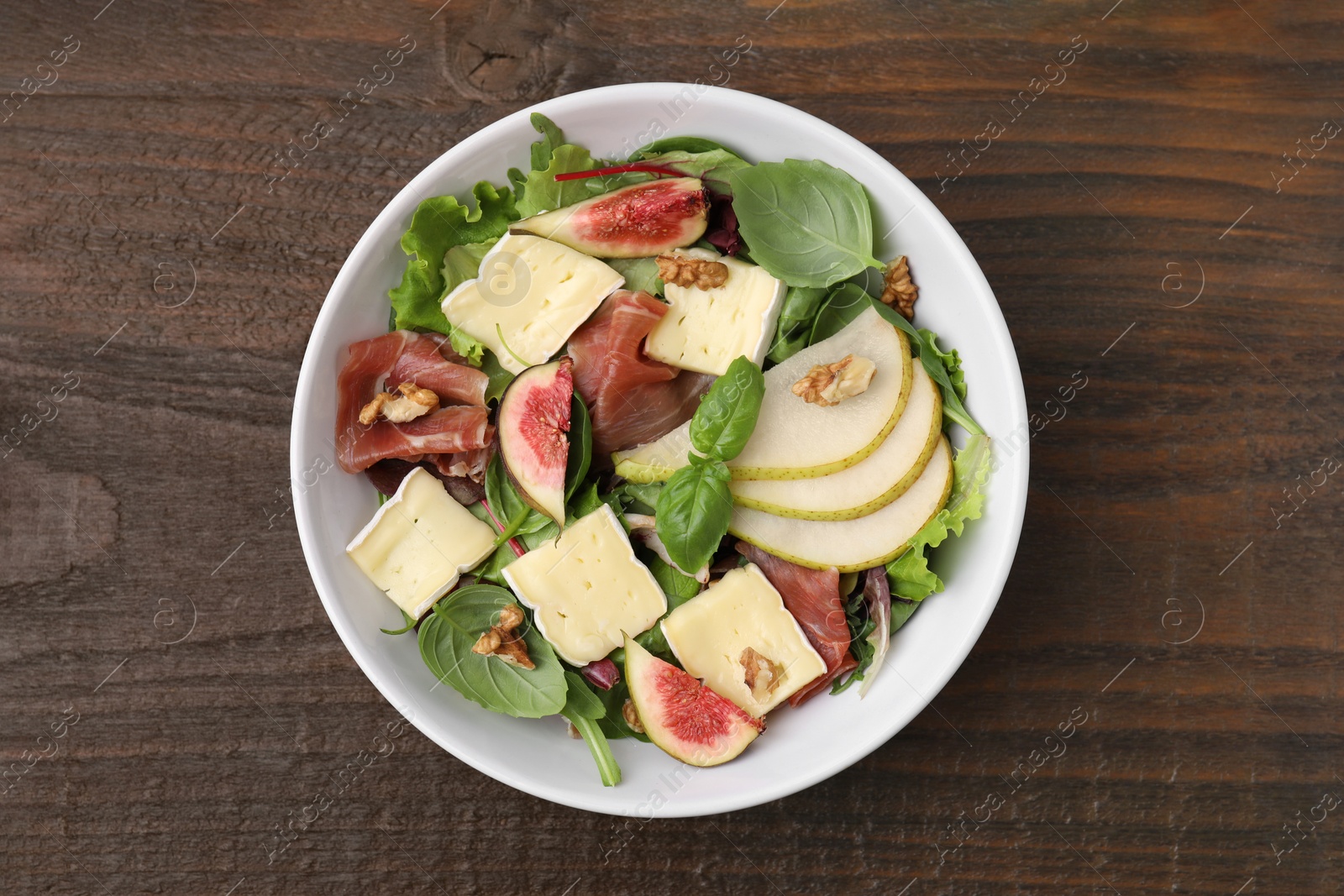 Photo of Tasty salad with brie cheese, prosciutto, pear and figs on wooden table, top view