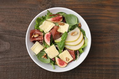 Tasty salad with brie cheese, prosciutto, pear and figs on wooden table, top view