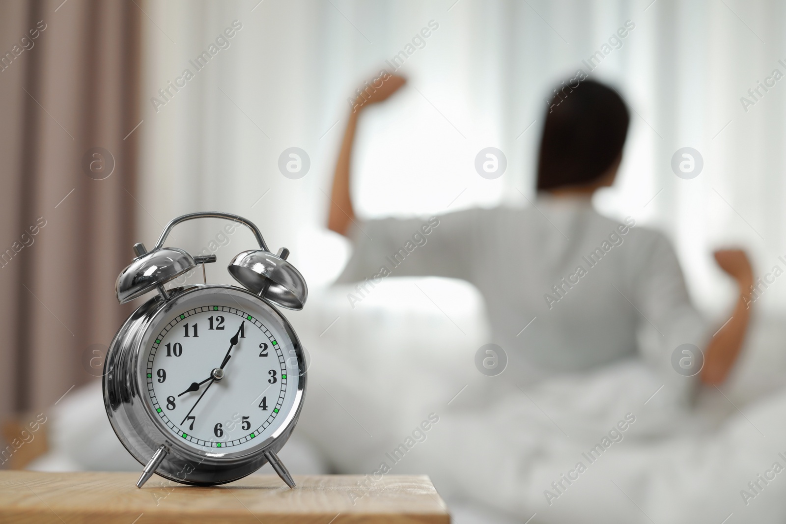 Photo of Woman stretching in bedroom, focus on alarm clock. Space for text