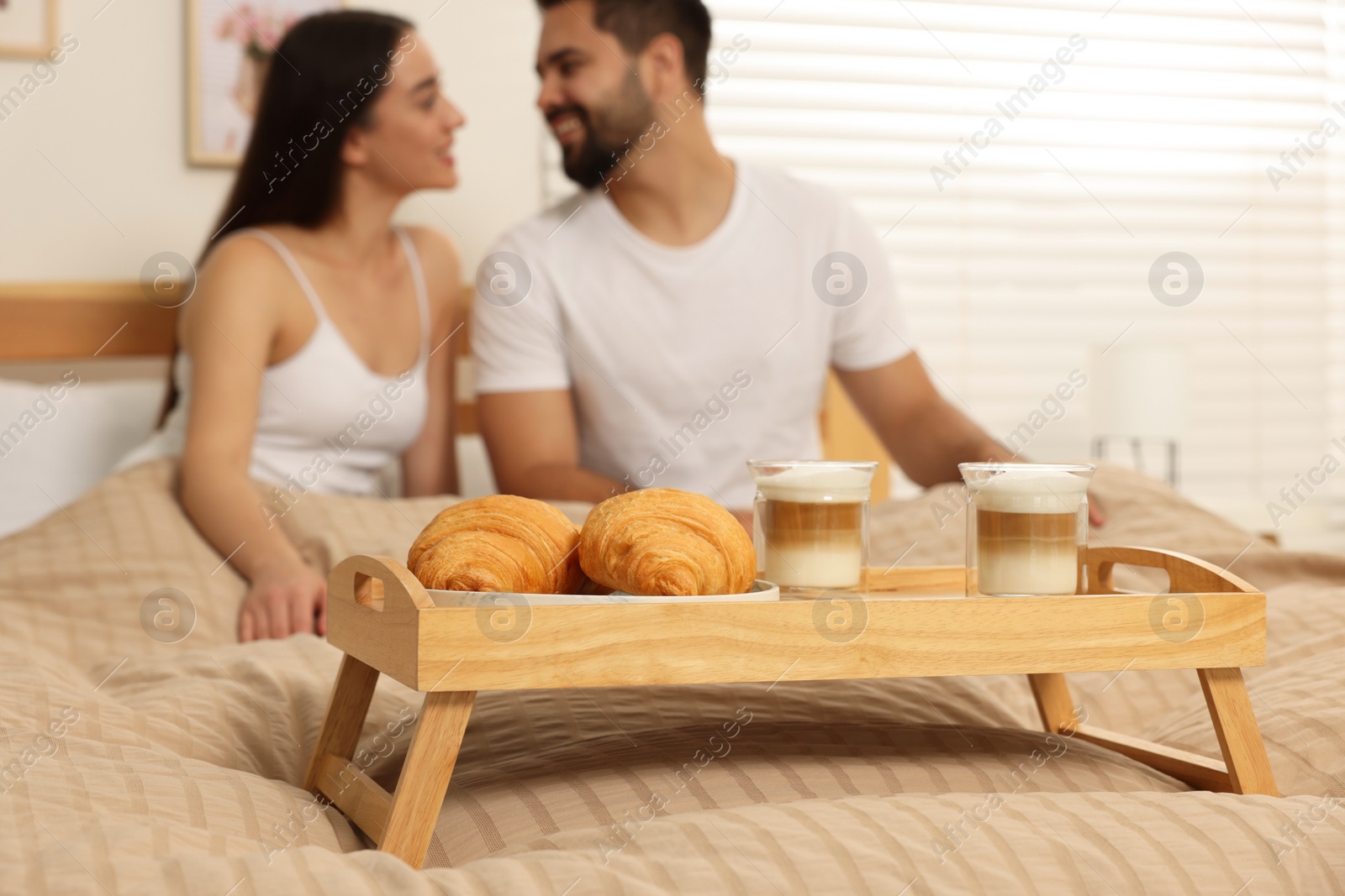 Photo of Happy couple together on bed at home, focus on wooden tray with breakfast